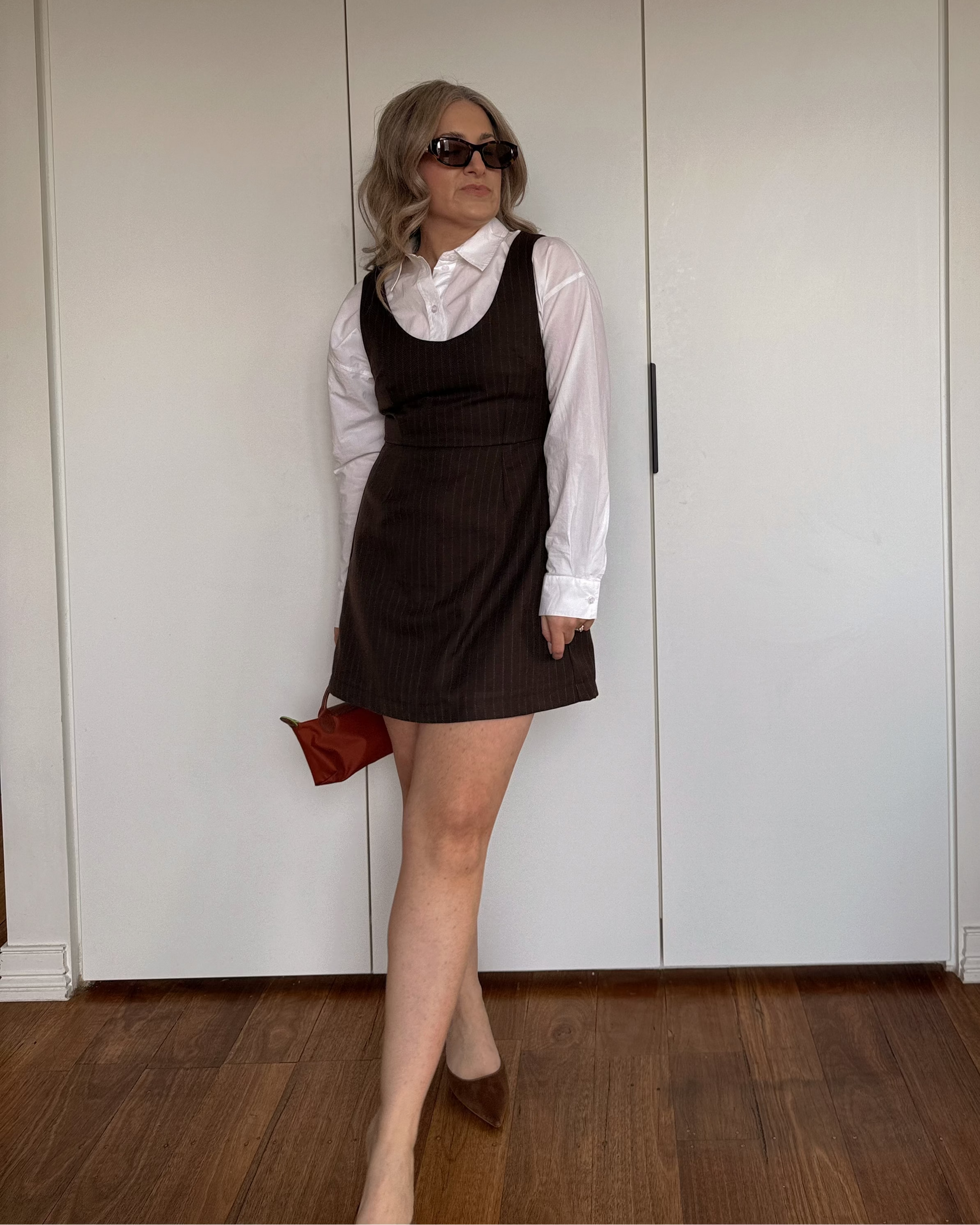 Model wearing the By Bel Pinstripe Espresso Mini Dress with a white collared shirt layered underneath.