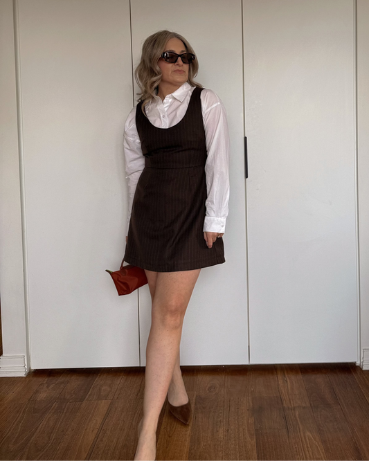 Model wearing the By Bel Pinstripe Espresso Mini Dress with a white collared shirt layered underneath.