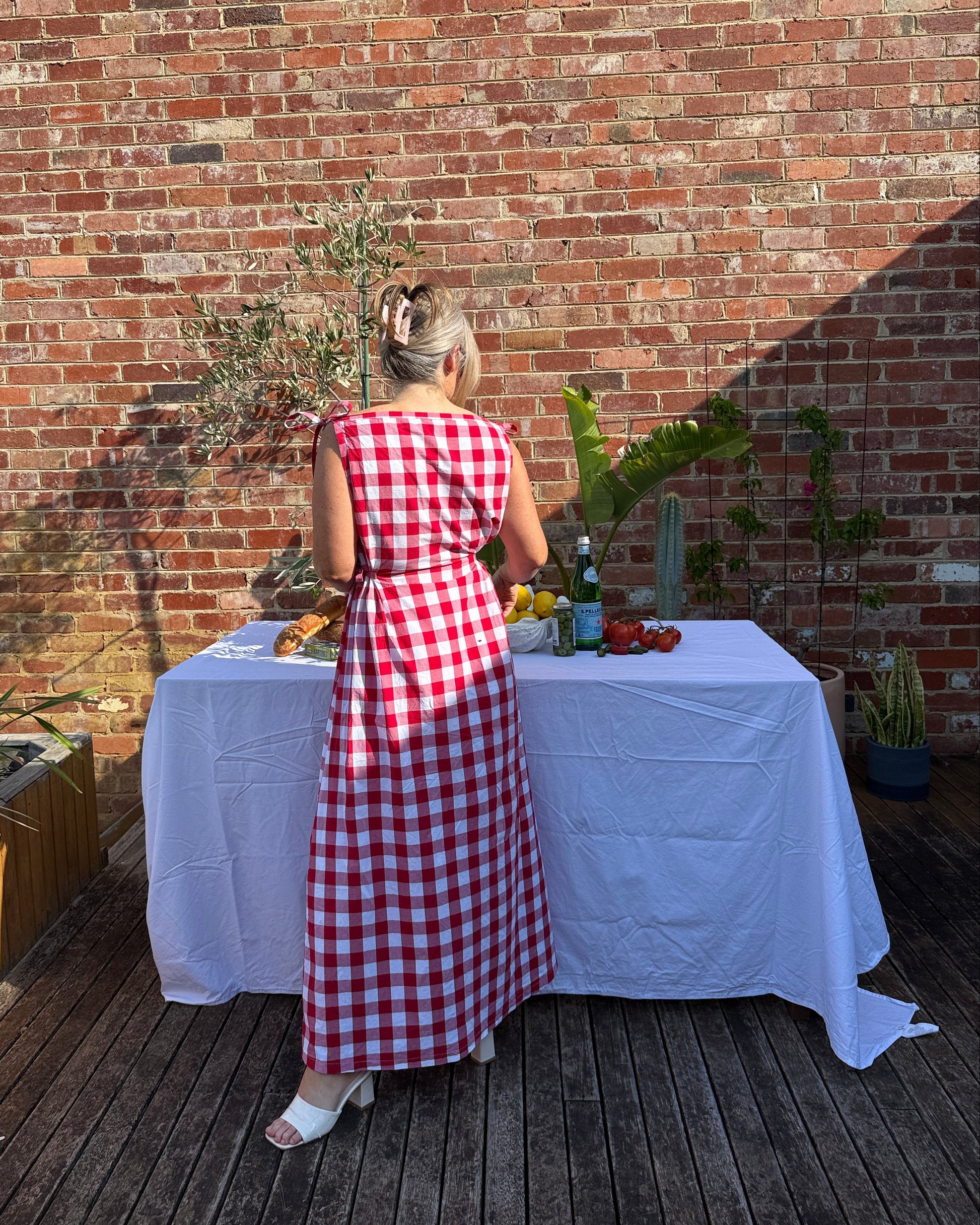 Back view of red gingham maxi dress by By Bel with flowing silhouette and adjustable tie waist for relaxed summer fit.